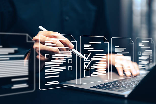 istock Digital document checklist and online form completion: Close-up of a hand using a stylus on a tablet to interact with holographic checklist boxes and digital document icons above a laptop. This conceptual image illustrates online surveys, digital forms. 2221601958