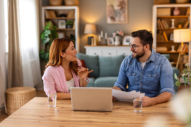 istock Couple is sitting at a table, focused on a laptop screen. They be discussing or working together, highlighting themes of collaboration, technology, and modern lifestyle in a home office setting 2221604792