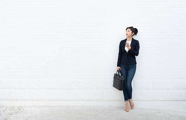 istock Smiling woman using mobile phone in front of white wall 2221616669