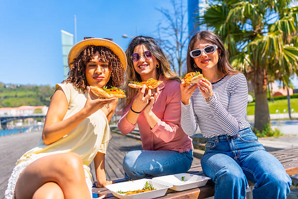 istock Young women eating pizza outdoors in urban setting 2221617256