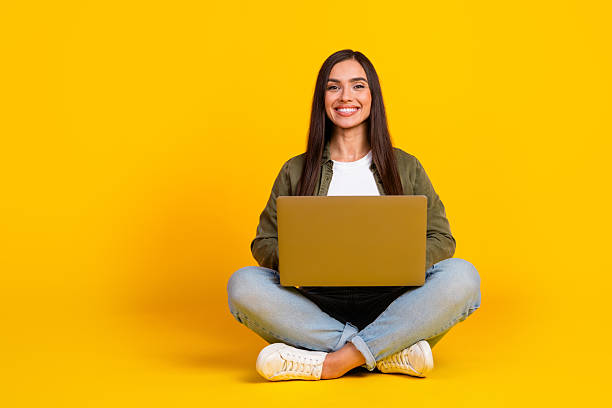istock Smiling woman sitting cross-legged using a laptop computer with yellow background expressing joy and relaxation 2221617598