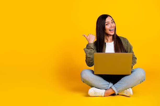 istock Cheerful young woman using a laptop on a bright yellow background while gesturing with her hand and smiling excitedly 2221617599