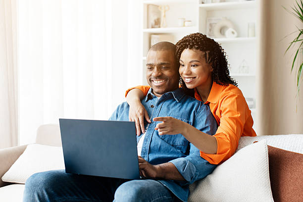 istock Black couple sitting on cozy sofa at home, using laptop together 2221618172
