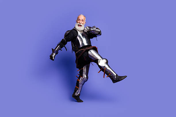 istock Cheerful elderly man in medieval armor kicking joyfully against a bold violet background. 2221618548