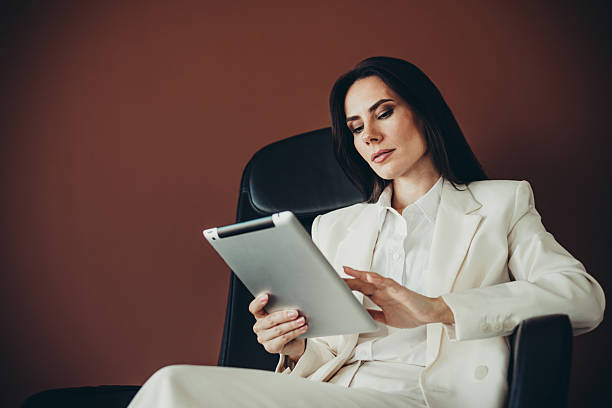 istock Professional businesswoman in an elegant white suit using a digital tablet while seated in an office environment 2221620952