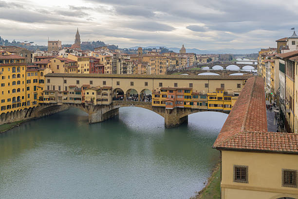 Panoramic view of Ponte Vecchio spanning the Arno River with Vasari Corridor and colorful medieval buildings in Florence, Italy.