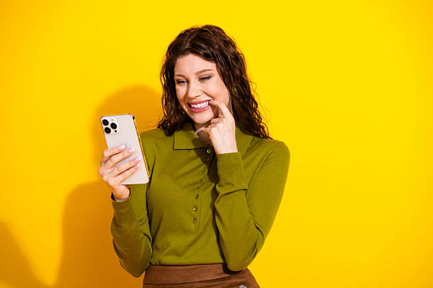 istock Young woman smiling while using smartphone against vibrant yellow background wearing trendy green shirt 2221622890