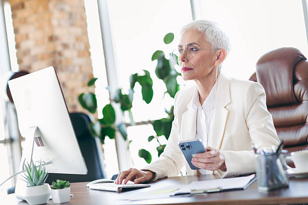 istock Professional businesswoman with short white hair working in a modern office using a computer and smartphone 2221623176