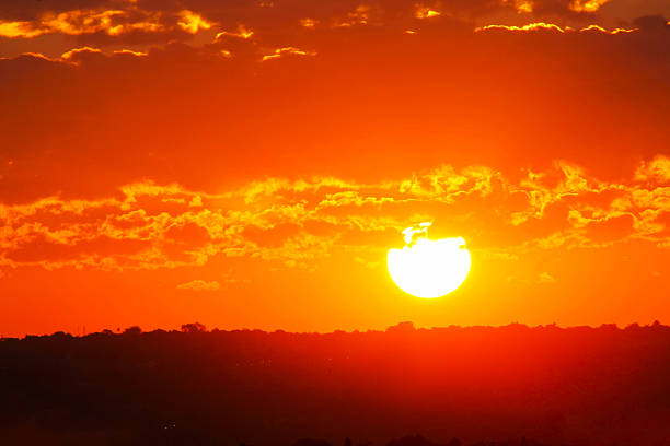 istock A blazing orange sunset descends behind a darkened horizon, illuminating scattered clouds with vibrant golden light. 2221628292