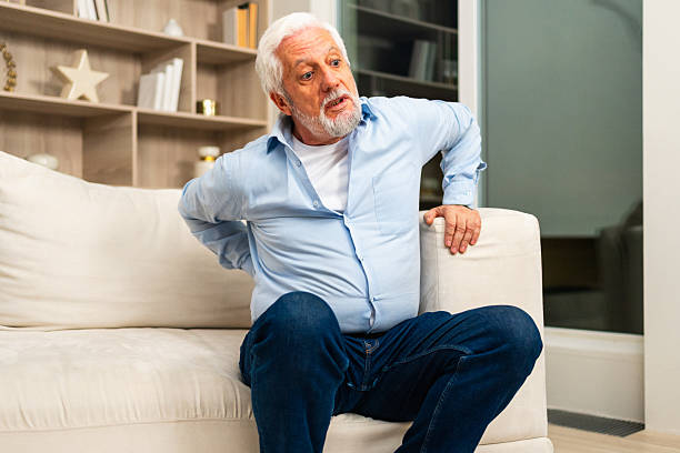 istock Backache back pain. Unhappy senior old man suffering from backache at home. Upset elder man feel sudden back pain muscles ache tension injury. Sad grandfather feeling pain hurt in back touching spine. 2221631797