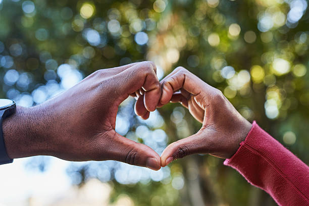 istock Couple Creating Heart Shape with Hands Outdoors in Sunlit Park, Symbolizing Love and Connection 2221634651