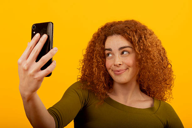 istock Redhead model taking a selfie with smartphone on yellow background 2221638975