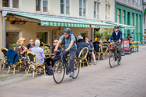 Strøget, Pedestrian Zone, Copenhagen, Zealand, Denmark - June18th 2025: Two middle-aged men wearing bike helmets ride down a pedestrian street on a sunny summer day. This is a common sight in the Danish capital, where many people have opted out of driving to avoid sitting in traffic, and cyclists and pedestrians usually coexist peacefully.