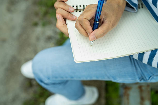 istock Close-up of woman's hand writing in notebook outdoors. Self-reflection, goal setting, journaling habit, and mindful planning. Creativity, life planning, and focus on personal growth. Mindful practice. 2221652096