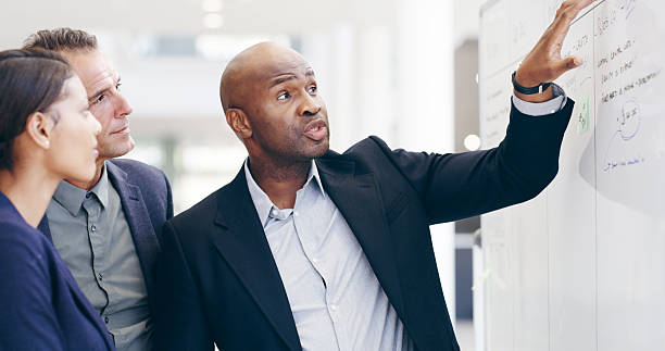 istock Discussion, planning or business people in meeting with whiteboard, schedule or project management. Agenda, list or team with timeline for brainstorming for progress, development or company resources 2221653140