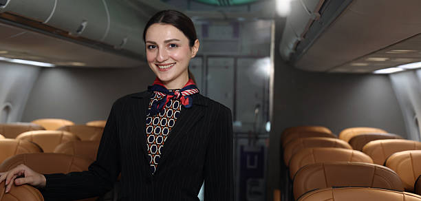 istock Air hostess. Smiling flight attendant in uniform welcomes and guides passengers aboard a modern airplane. Friendly airline staff providing professional service and comfortable travel flight experience 2221657596