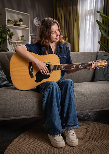 istock Young Woman Playing Acoustic Guitar on Comfortable Sofa 2221662572