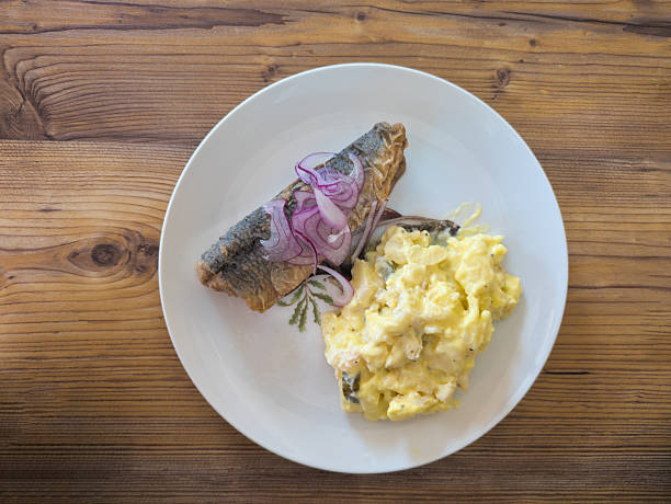 Fried herring with onions and potato salad served on plate, top view