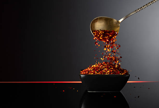 Dry chili pepper flakes in a small ceramic bowl on a black reflective background. Red pepper flakes pour in black bowl. Copy space.