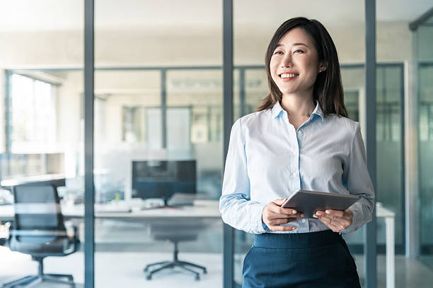 istock Smiling businesswoman CEO holding digital tablet using fintech tab online for work standing in modern office. Dreaming thoughtful portrait of mature Asian woman business female manager. Copy space 2221669885