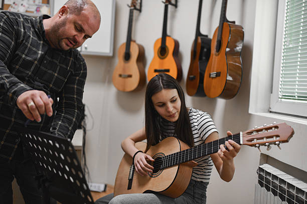 istock Girl Playing Guitar With Intense Focus While Male Instructor is Looking On With Interest 2221671924
