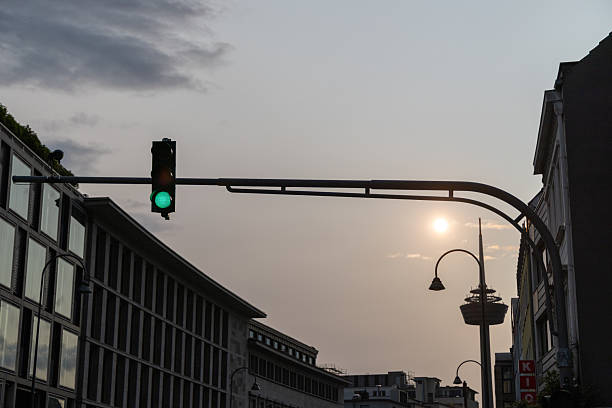 Urban scene with green traffic light against sunset sky and silhouette of city buildings.