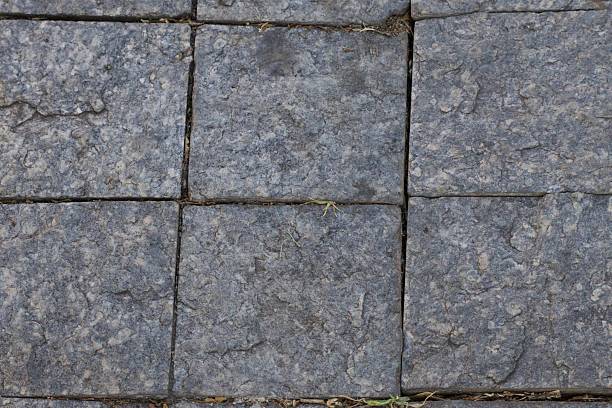 A gray stone wall with a few cracks in it. The wall is made up of square blocks