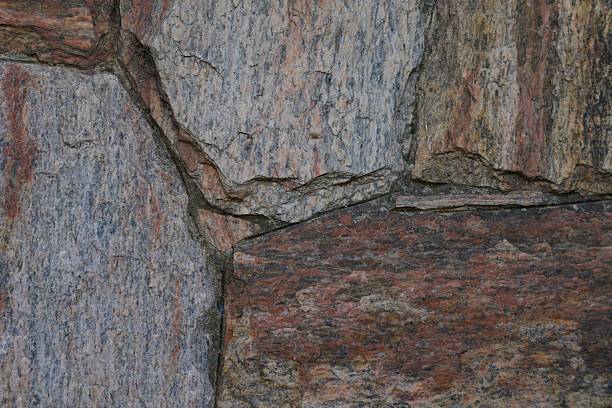 A stone wall with a red and gray color. The wall is made of stone and has a rough texture