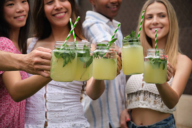 Group of friends holding glass jars with lemonade, mint and green and white striped straws, toasting