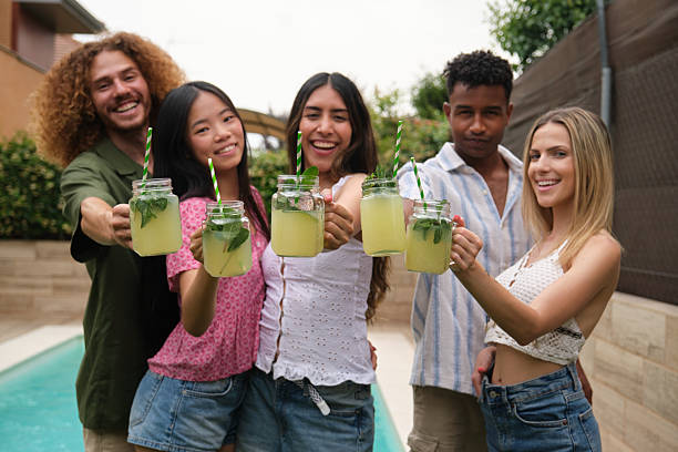 Group of cheerful multi-ethnic friends toasting with lemonade by the pool during a summer party