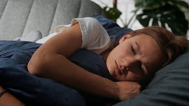 Woman Resting Uncomfortably on a Cozy Bed in Private Space