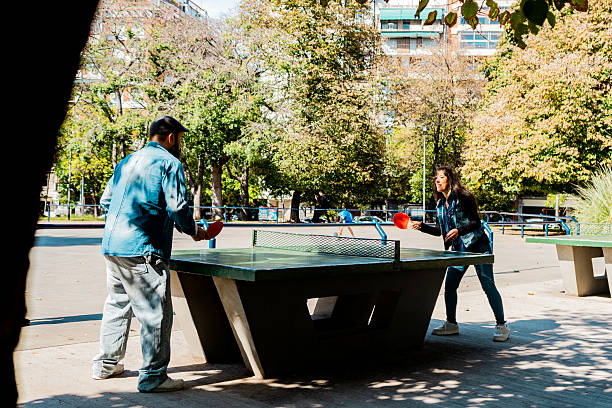 Friends playing table tennis on a public concrete table in a city park, enjoying a sunny day outdoors