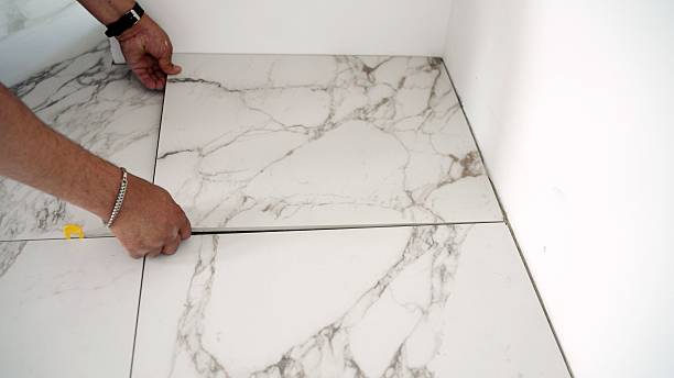 istock Tiler installing large white marble effect porcelain tiles 2221694565