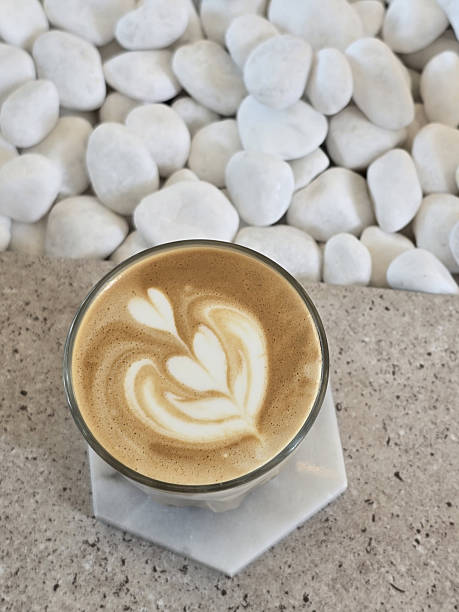 istock beautifully crafted latte with intricate foam art sits on marble surface, surrounded by smooth white pebbles, creating serene and inviting atmosphere 2221695409