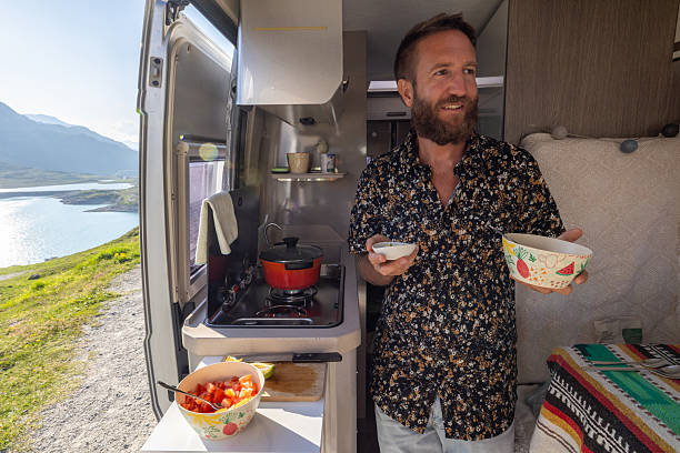 istock Man Enjoying Meal Prep Inside Camper Van with Scenic Lake View 2221695876