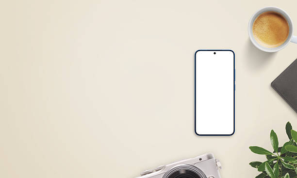 Smartphone mockup on beige desk with large empty space on left for promo text. Surrounded by coffee, camera, notebook, and plant