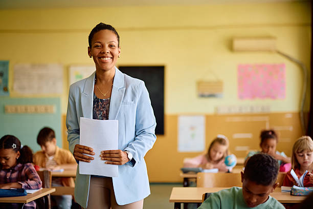 istock Happy black elementary school teacher among her students in the classroom looking at camera. 2221704393