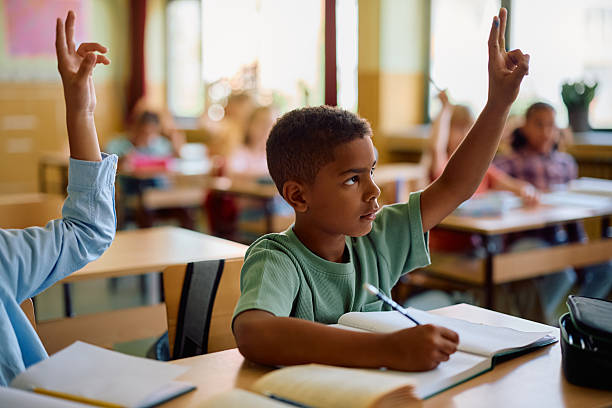 istock Black schoolboy raising hand to answer a question in the classroom. 2221704433