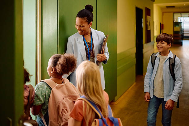 istock Happy black teacher greeting elementary students in front of the classroom. 2221704657