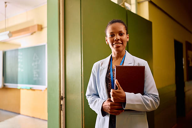 Smiling African American teacher waiting her students in front of the classroom on first day of school and looking at camera. Copy space.