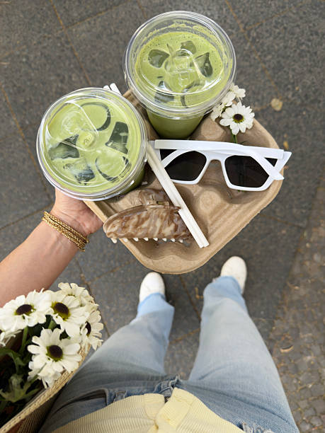 Woman holding a tray with two matcha lattes and sunglasses, creating user-generated content for social media