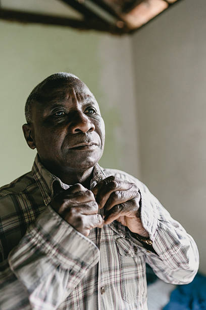 Elderly man adjusting shirt in poor living space