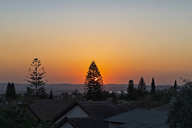 Sunset Over Residential Area with Silhouetted Trees and Mountains in Israel