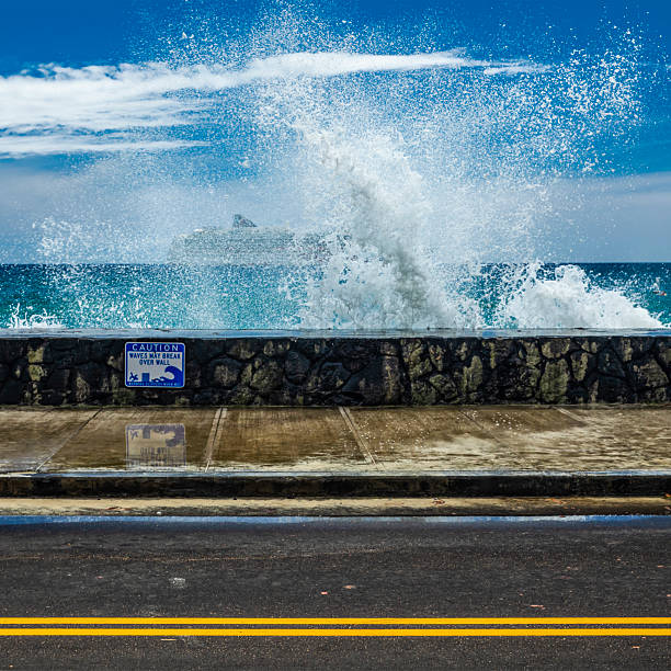 Kailua-Kona, Hawaii, Big Island, wave crashing against the seawall along  the Alii Drive sidewalk, warning sign about possible waves, cruise ship barely visible through the wave.