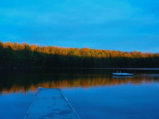 A peaceful lake scene at sunset with golden trees, a swim platform, and soft reflections on the water.