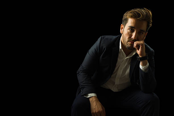 istock Pensive businessman sitting in studio with hand on chin 2221769000