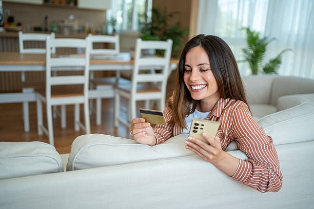 istock Smiling woman using smartphone and credit card on sofa at home 2221771814