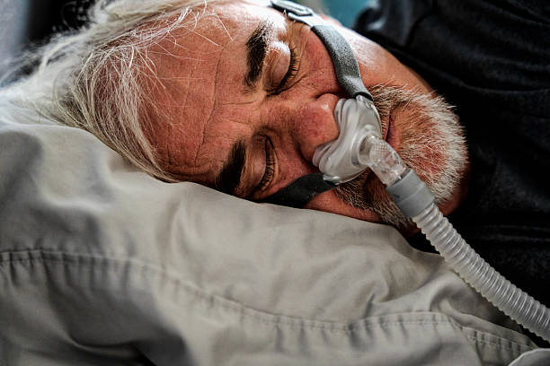 istock A 60-year-old man sleeps with a CPAP machine in bed. The machine helps him breathe better by delivering air pressure through a mask, improving sleep quality and reducing snoring. 2221771968