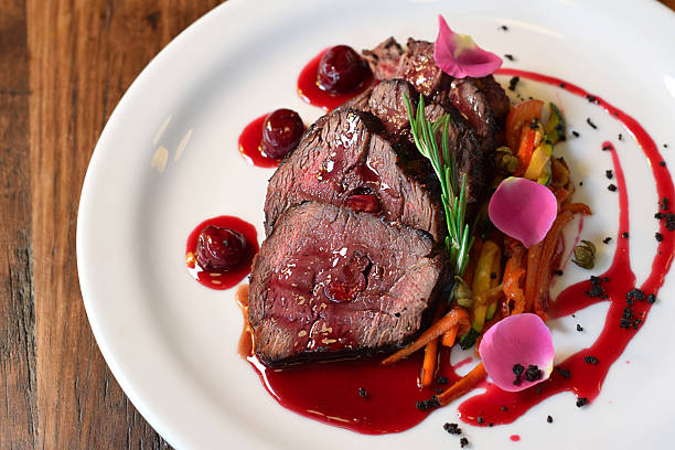 Top view sliced cooked veal served with julienne vegetables and cherry sauce, garnished with rosemary sprig