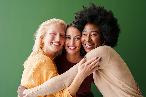 istock Three Diverse Friends Smiling Brightly in Warm Embrace Against a Vibrant Green Backdrop 2221779901
